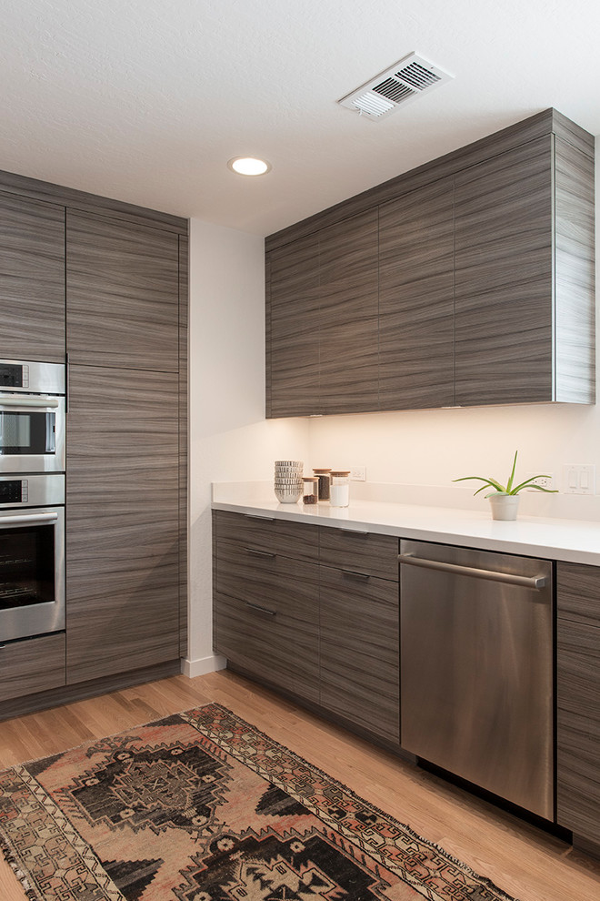 Photo of a mid-sized modern l-shaped eat-in kitchen in San Francisco with an undermount sink, flat-panel cabinets, dark wood cabinets, quartz benchtops, white splashback, stone slab splashback, stainless steel appliances, light hardwood floors, a peninsula, brown floor and white benchtop.