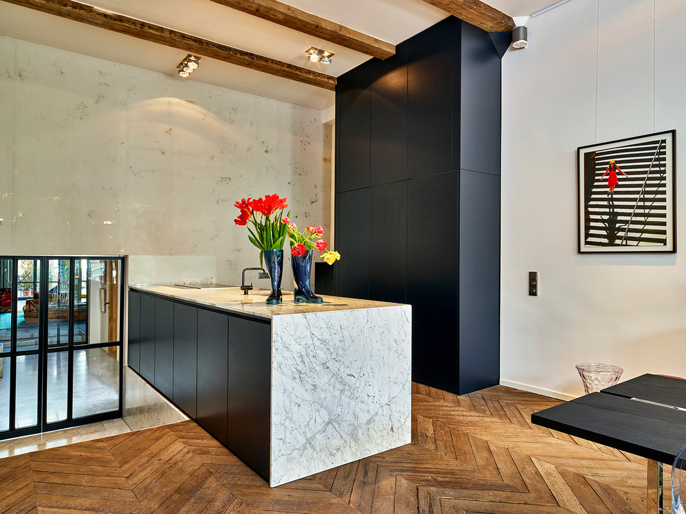 This is an example of an expansive contemporary galley open plan kitchen in Amsterdam with flat-panel cabinets, black cabinets, marble benchtops, medium hardwood floors and a peninsula.