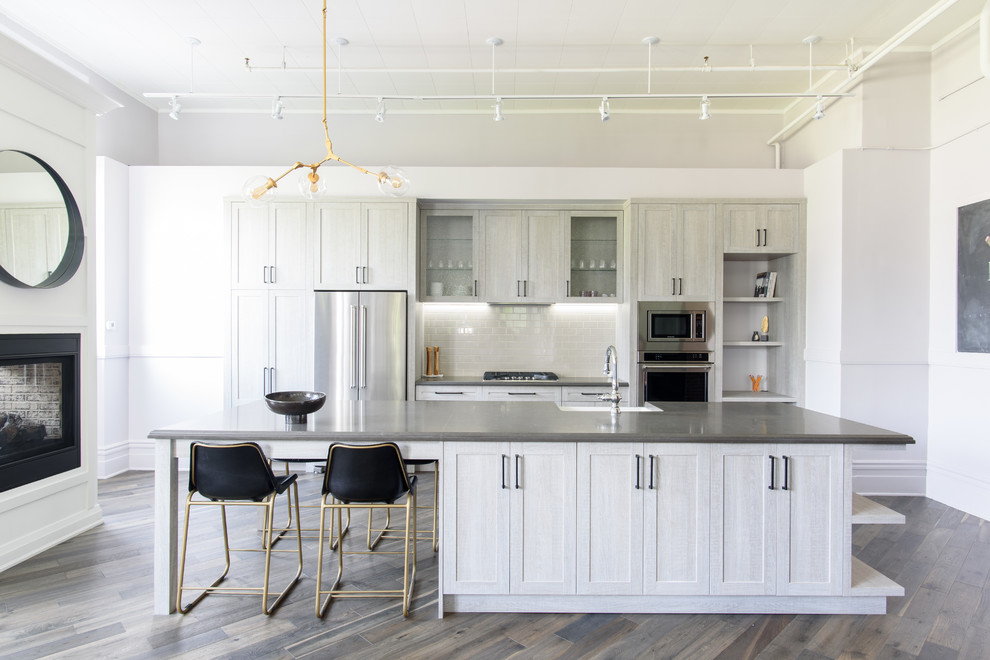 Inspiration for a transitional galley dark wood floor kitchen remodel in Toronto with a farmhouse sink, shaker cabinets, gray cabinets, white backsplash, subway tile backsplash, stainless steel appliances and an island