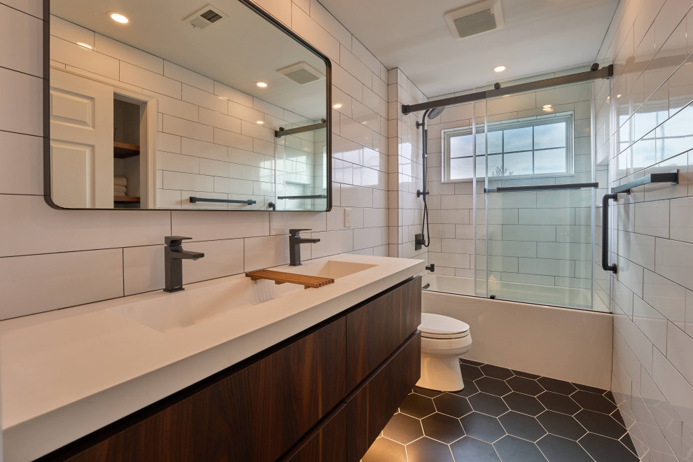 Mid-sized transitional kids bathroom in Philadelphia with flat-panel cabinets, dark wood cabinets, an alcove tub, a shower/bathtub combo, white tile, ceramic tile, white walls, ceramic floors, an integrated sink, engineered quartz benchtops, black floor, a sliding shower screen, white benchtops, a double vanity and a floating vanity.