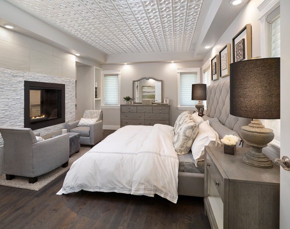 Design ideas for a transitional master bedroom in Edmonton with grey walls, dark hardwood floors, a two-sided fireplace and a tile fireplace surround.