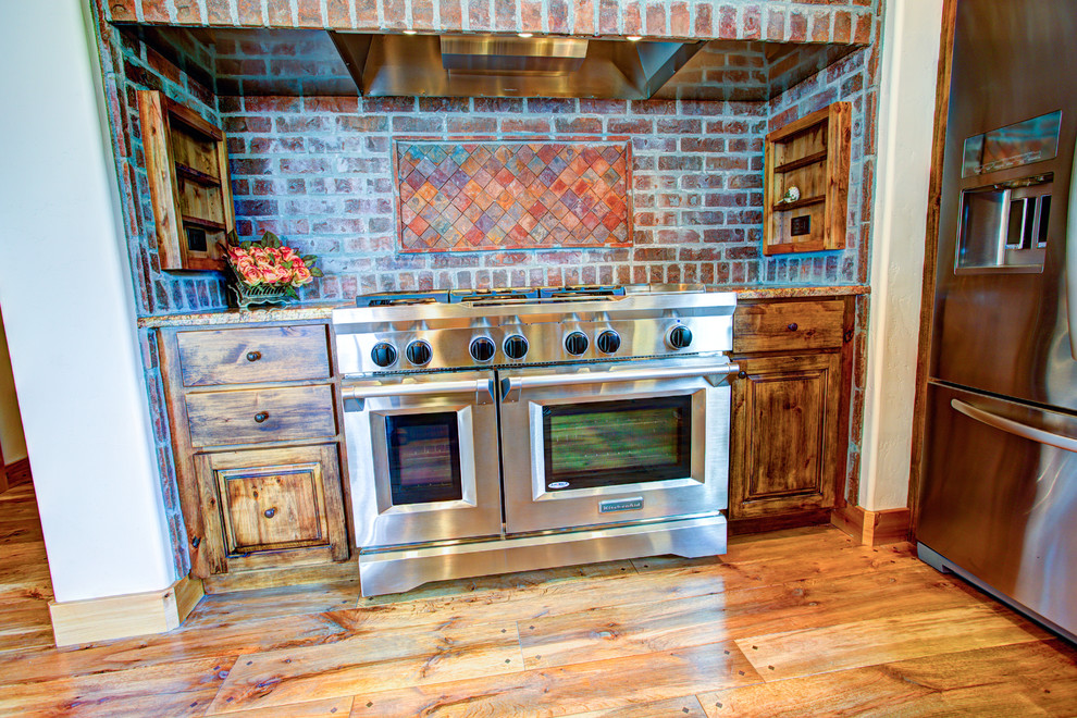 Kitchen pantry - large rustic u-shaped medium tone wood floor kitchen pantry idea with a drop-in sink, glass-front cabinets, medium tone wood cabinets, beige backsplash, stainless steel appliances and an island