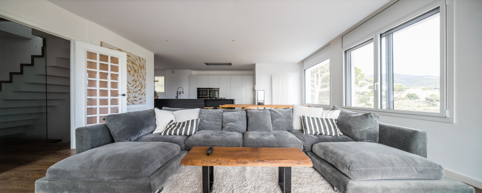 Großes, Offenes Modernes Wohnzimmer in grau-weiß mit weißer Wandfarbe, dunklem Holzboden, Gaskamin, verputzter Kaminumrandung, Multimediawand und braunem Boden in Barcelona