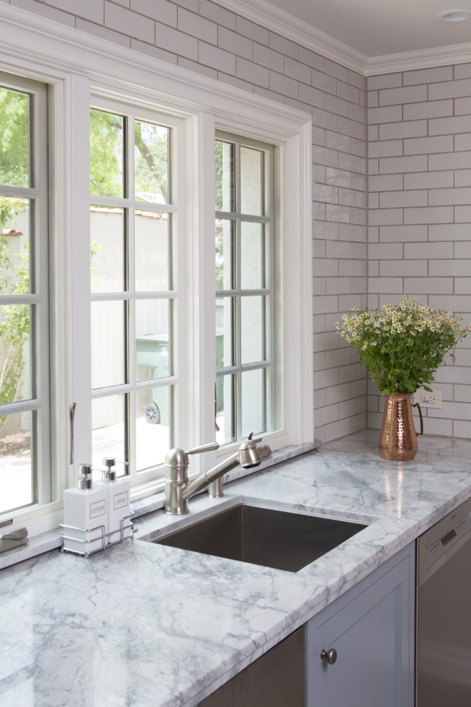 Large transitional u-shaped porcelain tile and gray floor enclosed kitchen photo in Los Angeles with a drop-in sink, shaker cabinets, quartzite countertops, white backsplash, ceramic backsplash, stainless steel appliances, an island and gray countertops