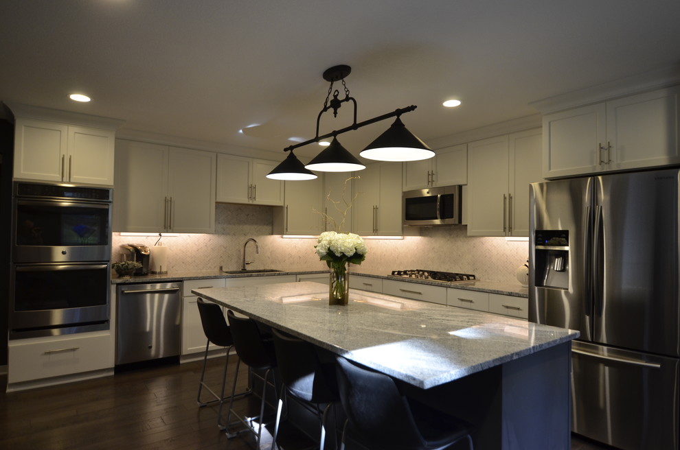 Example of a mid-sized transitional l-shaped dark wood floor and brown floor open concept kitchen design in Minneapolis with an undermount sink, flat-panel cabinets, white cabinets, granite countertops, white backsplash, ceramic backsplash, stainless steel appliances and an island