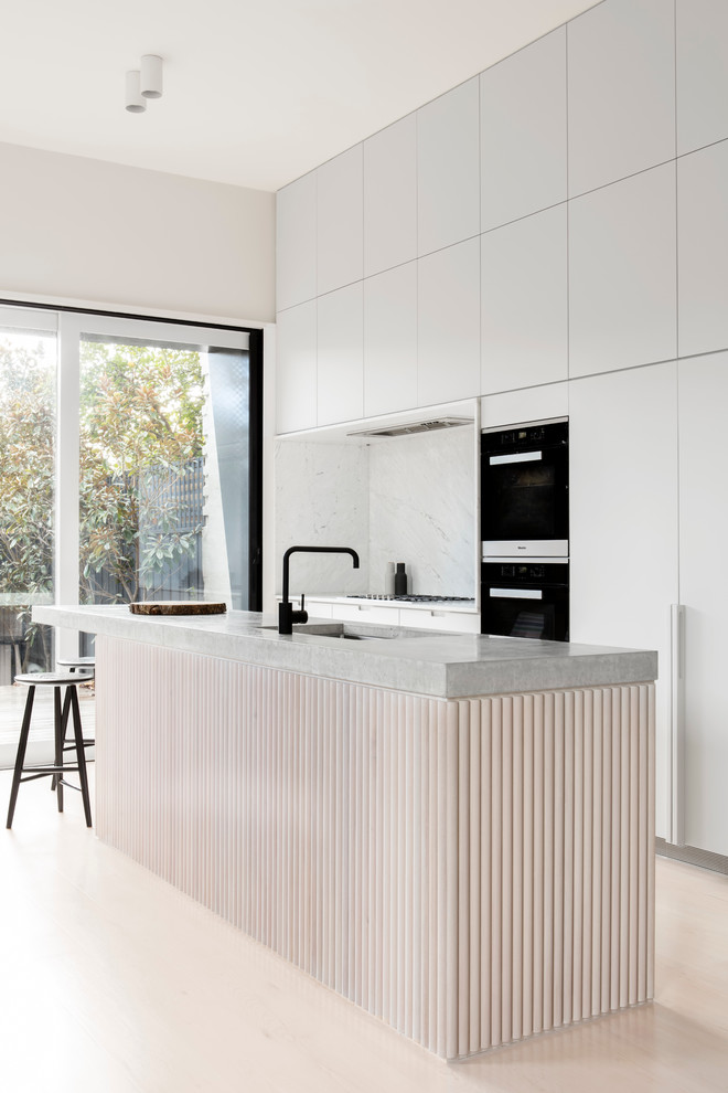 Mid-sized modern galley kitchen in Melbourne with an undermount sink, concrete benchtops, white splashback, stone slab splashback, black appliances, with island and flat-panel cabinets.