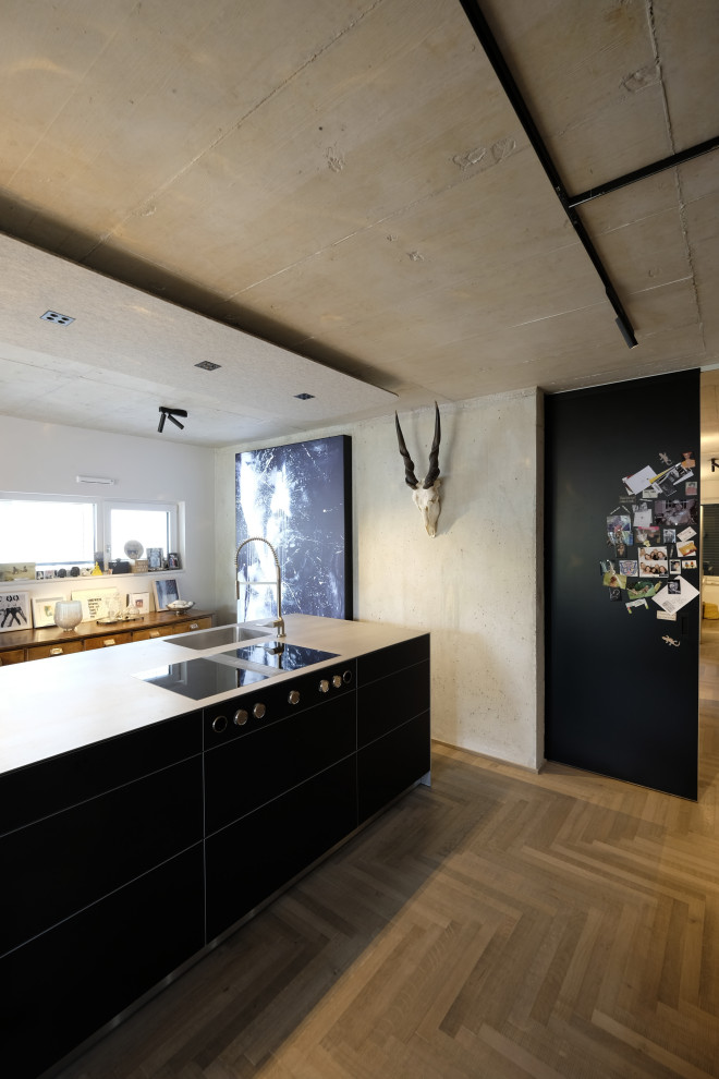Inspiration for an expansive industrial galley eat-in kitchen in Cologne with a single-bowl sink, flat-panel cabinets, black cabinets, stainless steel benchtops, black appliances, with island, grey floor and painted wood floors.