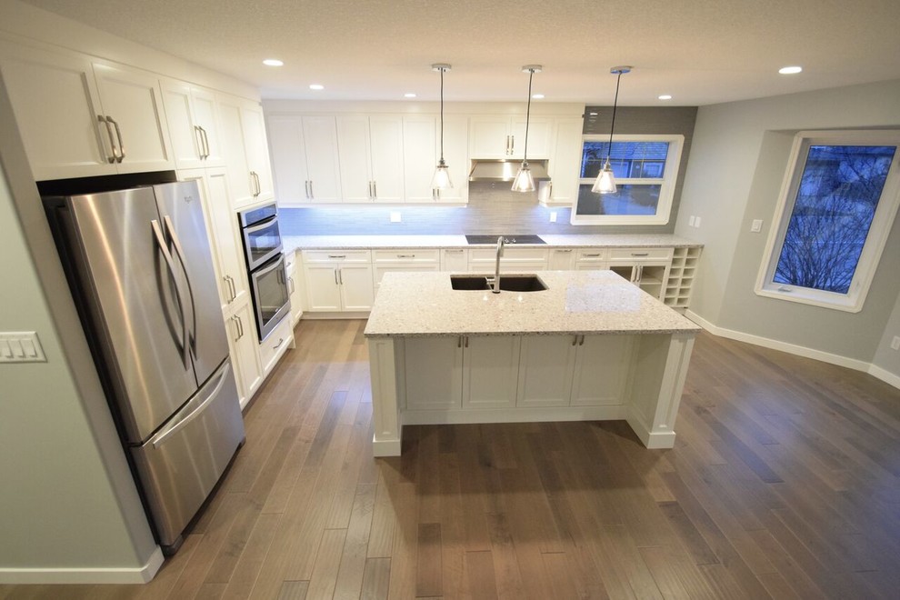 Eat-in kitchen - transitional l-shaped vinyl floor eat-in kitchen idea in Edmonton with a double-bowl sink, shaker cabinets, white cabinets, quartz countertops, gray backsplash, glass tile backsplash, stainless steel appliances and an island