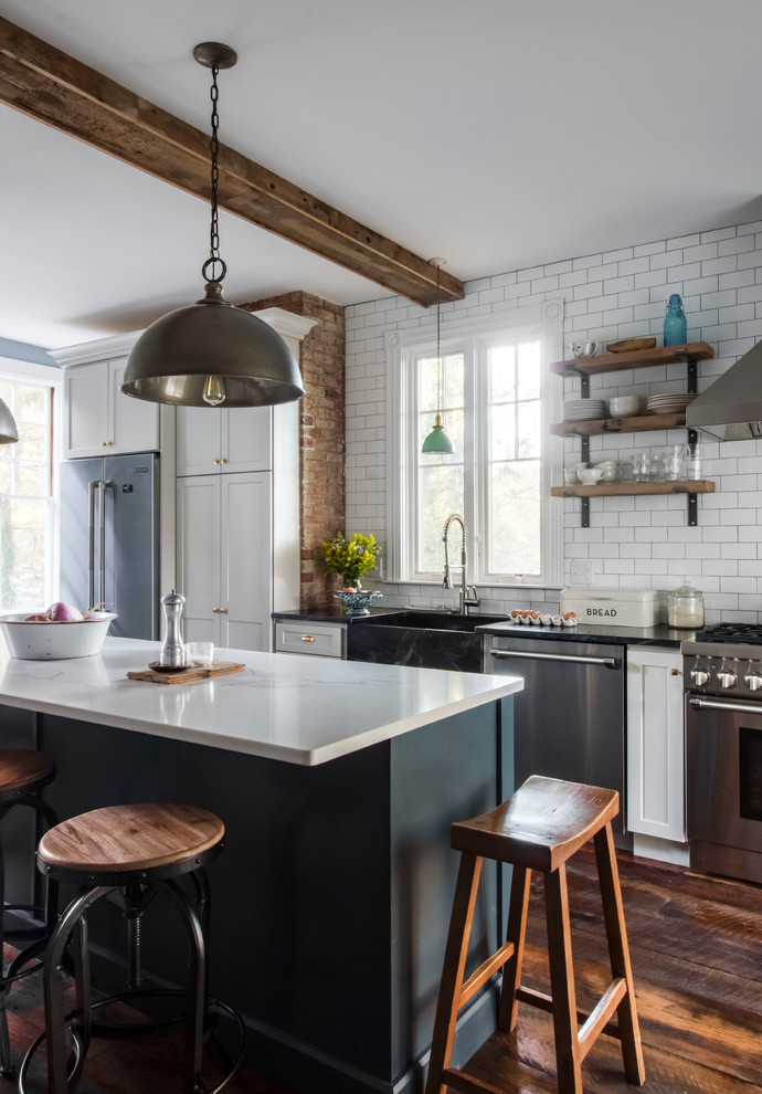 Photo of a mid-sized country single-wall separate kitchen in Boston with a farmhouse sink, flat-panel cabinets, white cabinets, soapstone benchtops, white splashback, porcelain splashback, stainless steel appliances, dark hardwood floors, with island and brown floor.