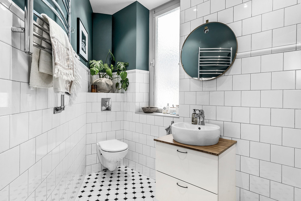 Inspiration for a mid-sized scandinavian bathroom in Copenhagen with flat-panel cabinets, white cabinets, a wall-mount toilet, white tile, wood benchtops and multi-coloured floor.