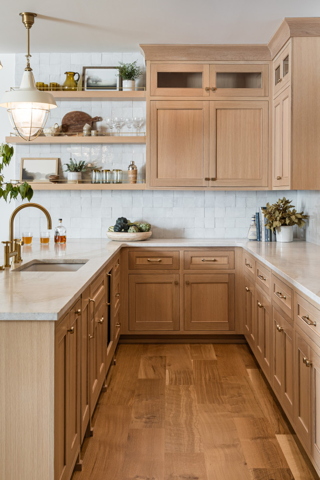 Flint Hills - Home bar - transitional u-shaped medium tone wood floor and brown floor home bar idea in Orange County with an undermount sink, recessed-panel cabinets, light wood cabinets, white backsplash and beige countertops