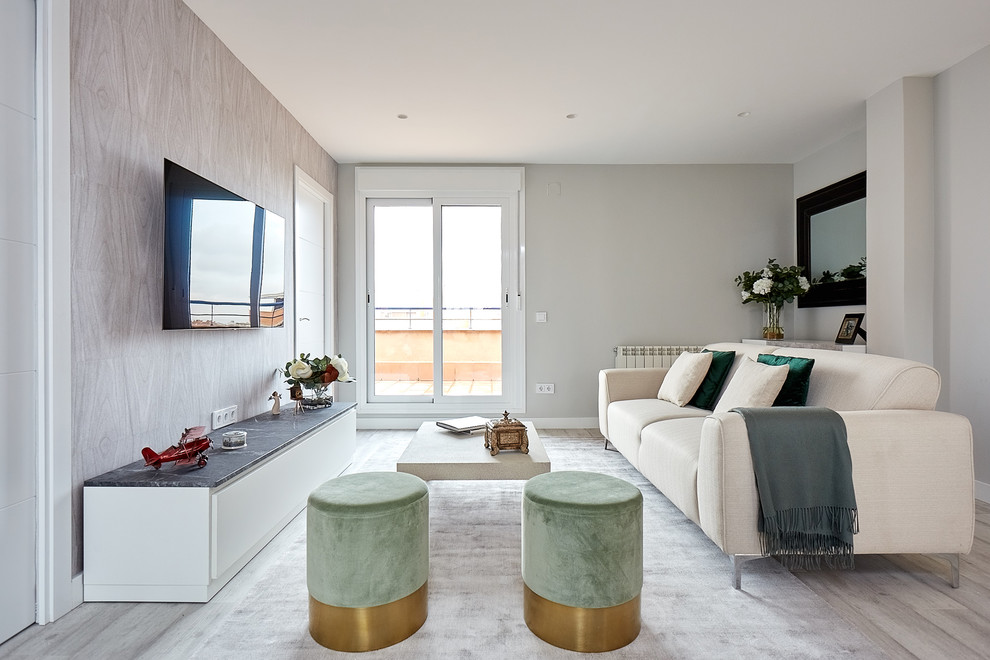 This is an example of a contemporary living room in Madrid with grey walls, light hardwood floors, a wall-mounted tv and grey floor.
