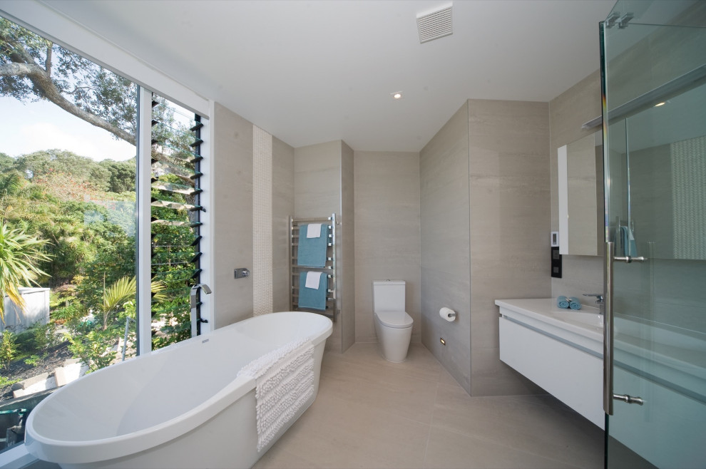 Идея дизайна: главная ванная комната среднего размера в морском стиле с фасадами островного типа, белыми фасадами, отдельно стоящей ванной, угловым душем, унитазом-моноблоком, бежевой плиткой, плиткой из листового камня, бежевыми стенами, монолитной раковиной, столешницей из искусственного кварца, разноцветным полом, душем с распашными дверями, белой столешницей, тумбой под две раковины и подвесной тумбой