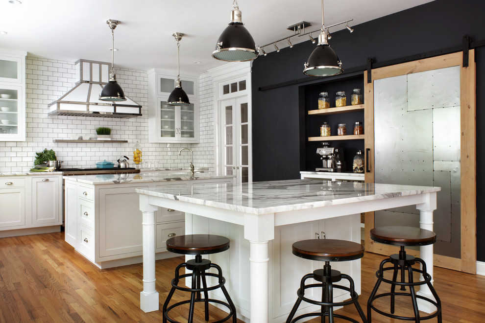 Design ideas for a large transitional l-shaped kitchen in New York with white cabinets, marble benchtops, white splashback, subway tile splashback, stainless steel appliances, multiple islands, white benchtop, an undermount sink, shaker cabinets and light hardwood floors.