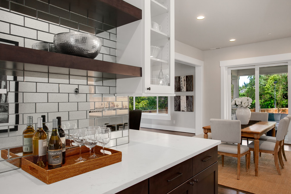 Photo of a large arts and crafts eat-in kitchen in Seattle with recessed-panel cabinets, white cabinets, quartz benchtops, metallic splashback, mirror splashback, dark hardwood floors, brown floor and white benchtop.