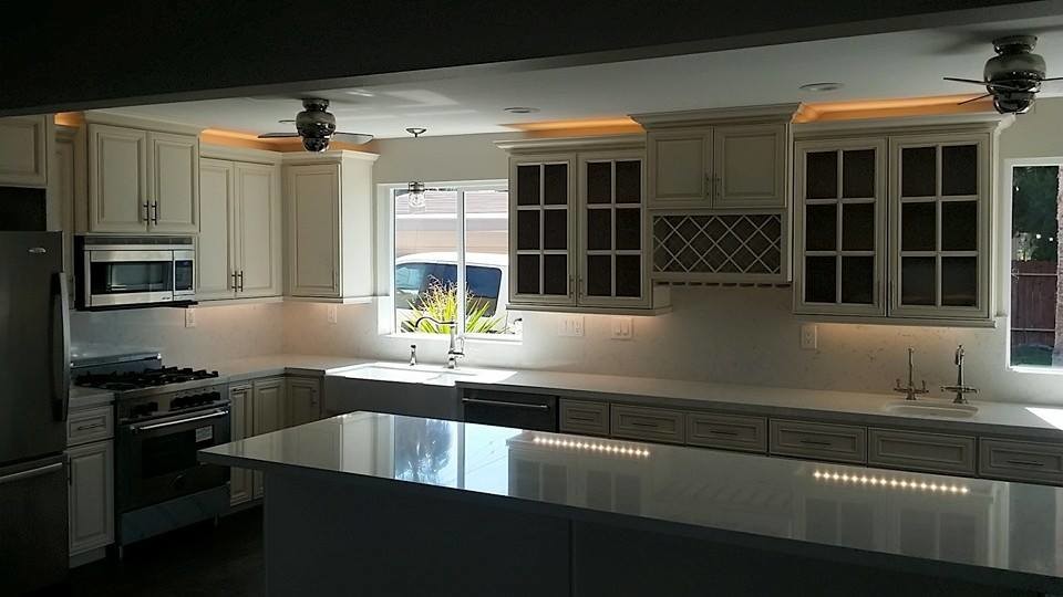 Large country l-shaped eat-in kitchen in Los Angeles with a farmhouse sink, shaker cabinets, white cabinets, solid surface benchtops, white splashback, stone slab splashback, stainless steel appliances and with island.