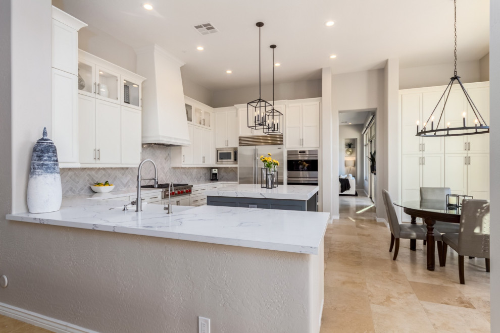 Example of a large transitional u-shaped travertine floor and beige floor eat-in kitchen design in Phoenix with a farmhouse sink, shaker cabinets, white cabinets, quartz countertops, gray backsplash, ceramic backsplash, stainless steel appliances, an island and white countertops