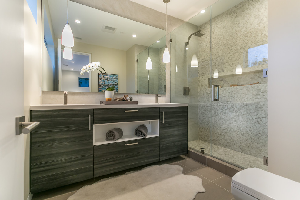 Photo of a modern bathroom in Los Angeles with a drop-in sink, flat-panel cabinets, grey cabinets, engineered quartz benchtops, a freestanding tub, an open shower, a one-piece toilet, brown tile, porcelain tile, white walls and medium hardwood floors.