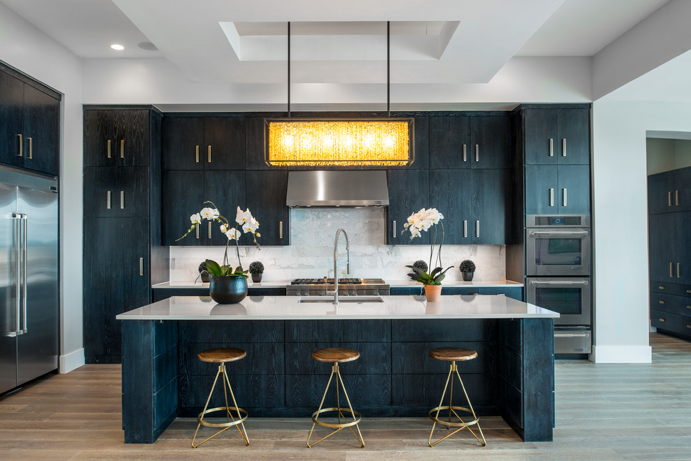 Photo of a contemporary l-shaped open plan kitchen in Austin with an undermount sink, flat-panel cabinets, black cabinets, quartz benchtops, white splashback, stone tile splashback, stainless steel appliances, medium hardwood floors and with island.