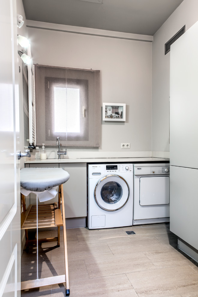 Design ideas for a small transitional u-shaped dedicated laundry room in Other with flat-panel cabinets, grey cabinets, solid surface benchtops, grey walls, limestone floors and a side-by-side washer and dryer.