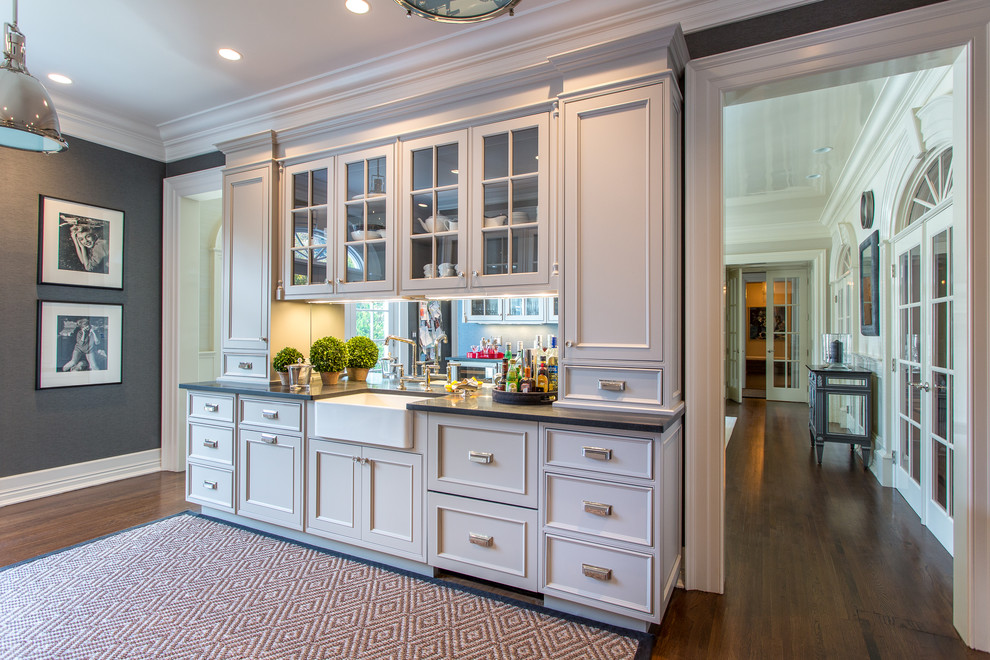 Small traditional single-wall wet bar in New York with beaded inset cabinets, white cabinets, solid surface benchtops, mirror splashback, dark hardwood floors and brown floor.
