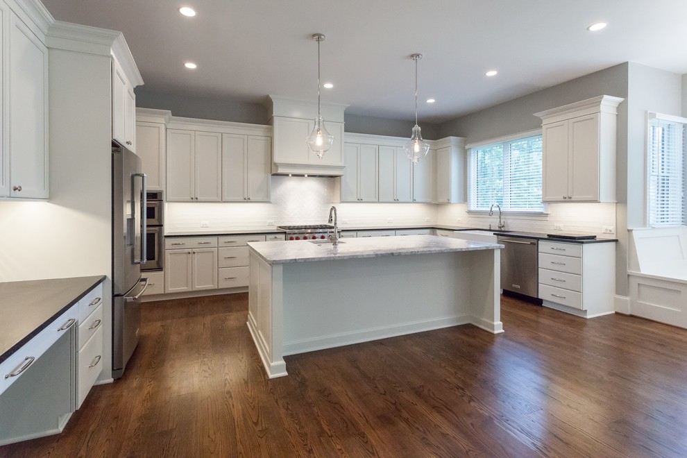 Transitional u-shaped medium tone wood floor and brown floor open concept kitchen photo in DC Metro with a farmhouse sink, recessed-panel cabinets, white cabinets, white backsplash, subway tile backsplash, stainless steel appliances, an island and black countertops