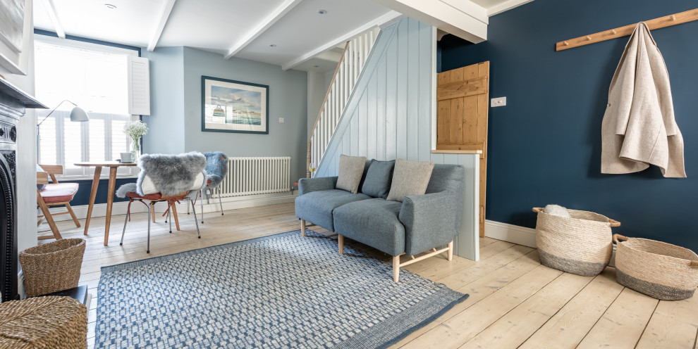 Kleines, Offenes Nordisches Wohnzimmer mit blauer Wandfarbe, hellem Holzboden, Kamin, Kaminumrandung aus Metall, freistehendem TV und freigelegten Dachbalken in Cornwall
