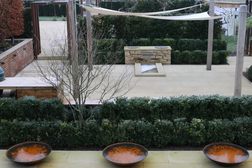 This is an example of a small contemporary courtyard patio in Hertfordshire with a water feature, natural stone pavers and an awning.