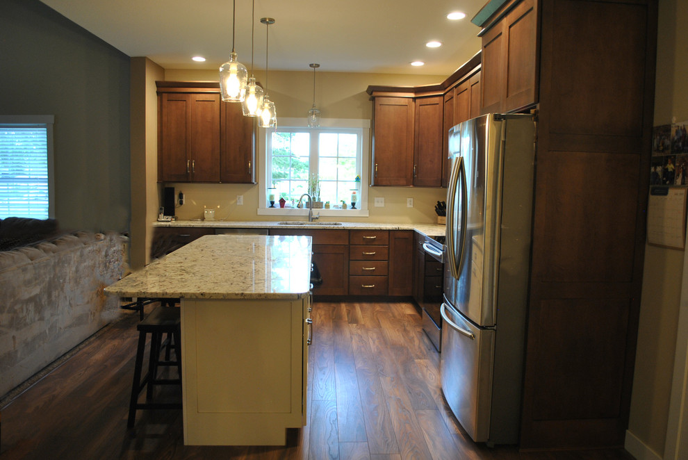 Example of a brown floor kitchen design with brown cabinets, stainless steel appliances, an island and beige countertops