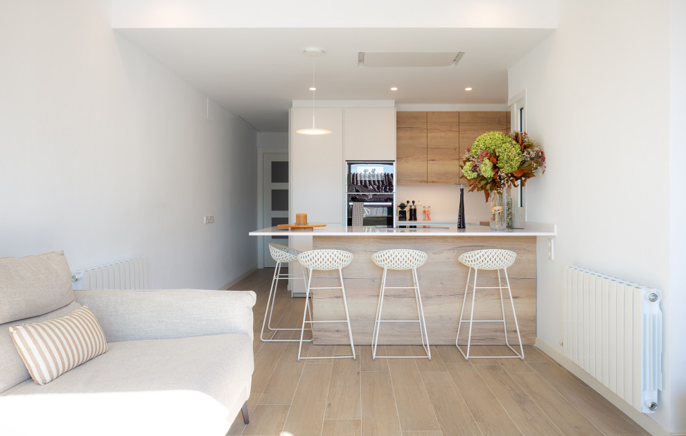 This is an example of a mid-sized mediterranean u-shaped open plan kitchen in Barcelona with a single-bowl sink, flat-panel cabinets, medium wood cabinets, beige splashback, black appliances, ceramic floors, a peninsula, brown floor, beige benchtop and recessed.