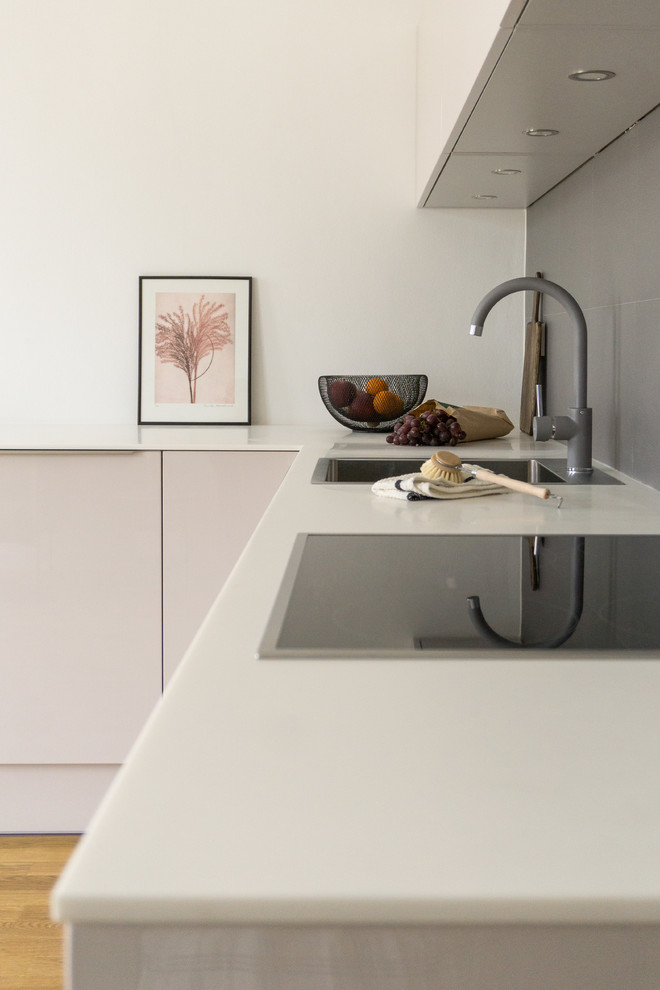 This is an example of a small modern l-shaped eat-in kitchen in Berlin with a drop-in sink, flat-panel cabinets, purple cabinets, solid surface benchtops, grey splashback, stone tile splashback, panelled appliances, medium hardwood floors, no island, brown floor and white benchtop.