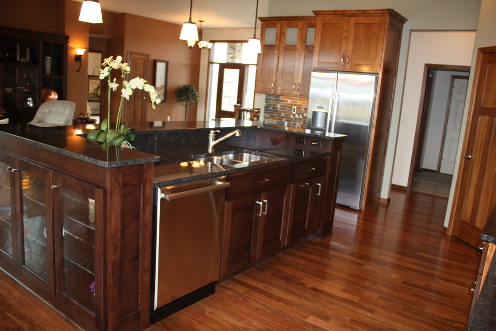 Example of a mid-sized transitional l-shaped medium tone wood floor home design design with an undermount sink, recessed-panel cabinets, medium tone wood cabinets, granite countertops, multicolored backsplash, mosaic tile backsplash, stainless steel appliances and an island