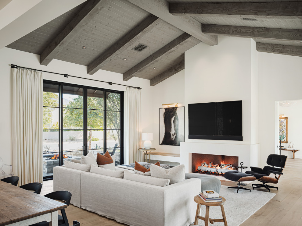 Foto de salón abierto minimalista con paredes blancas, suelo de madera clara, chimenea lineal, marco de chimenea de yeso, televisor colgado en la pared, suelo beige y vigas vistas