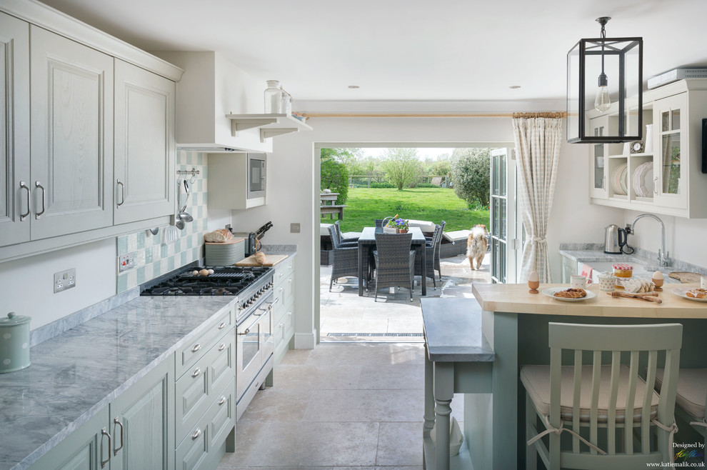 Photo of a transitional open plan kitchen in Cambridgeshire with a farmhouse sink, shaker cabinets, green cabinets, marble benchtops, ceramic splashback and limestone floors.