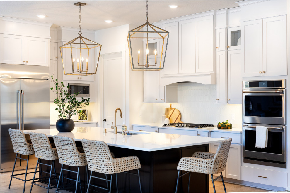 Inspiration for a transitional l-shaped kitchen in Minneapolis with an undermount sink, shaker cabinets, white cabinets, white splashback, stainless steel appliances, medium hardwood floors, with island, brown floor and white benchtop.