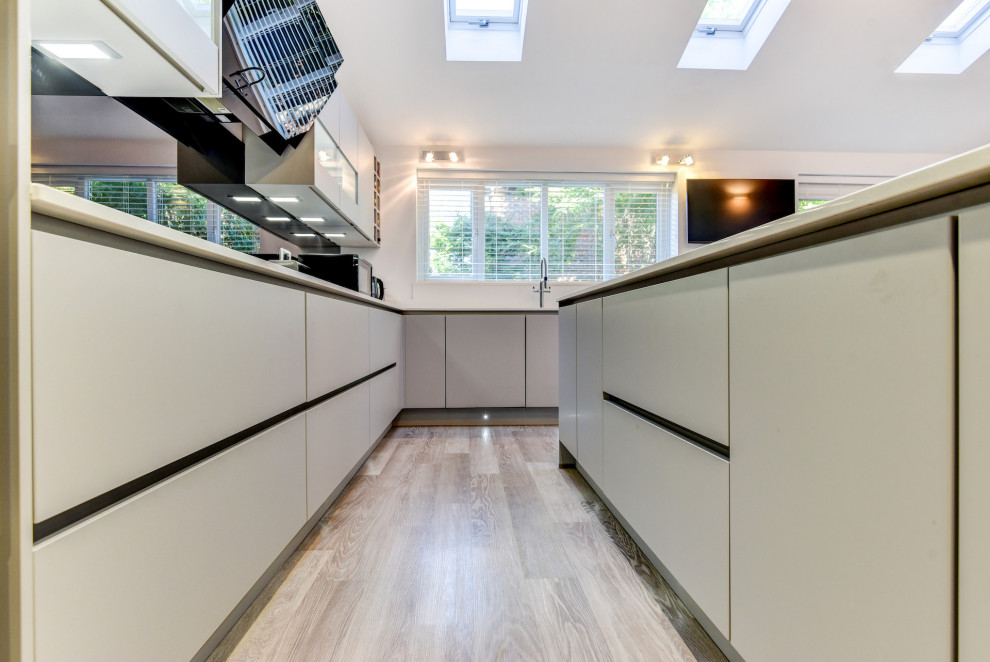 Large modern grey and white l-shaped kitchen/diner in Sussex with a submerged sink, flat-panel cabinets, grey cabinets, quartz worktops, black splashback, glass sheet splashback, black appliances, vinyl flooring, an island, grey floors, white worktops and feature lighting.