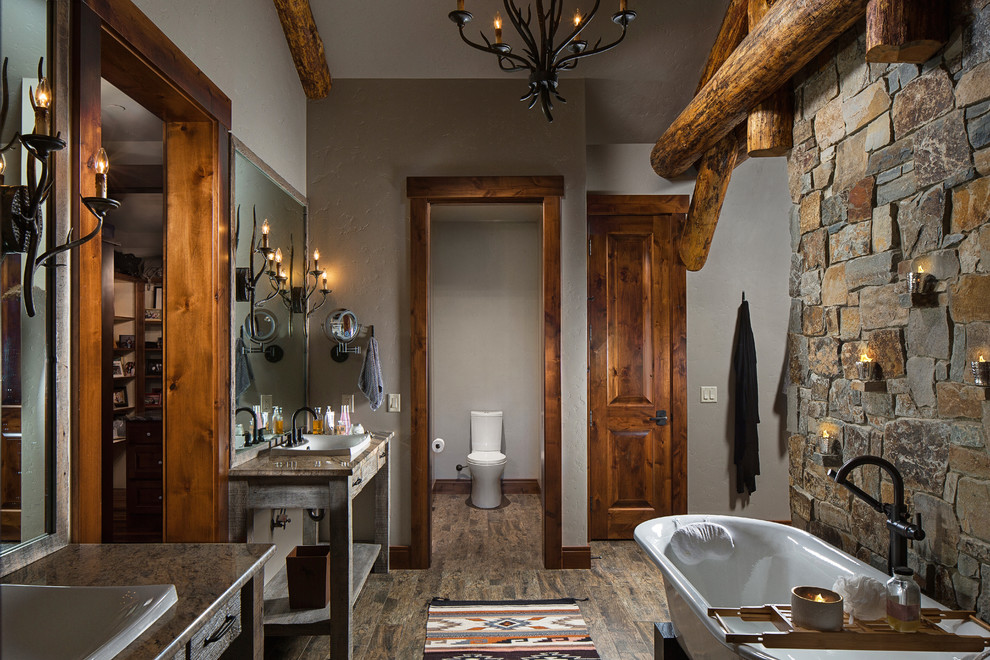 Freestanding bathtub - large rustic master dark wood floor freestanding bathtub idea with flat-panel cabinets, distressed cabinets, granite countertops, a two-piece toilet, gray walls and a vessel sink