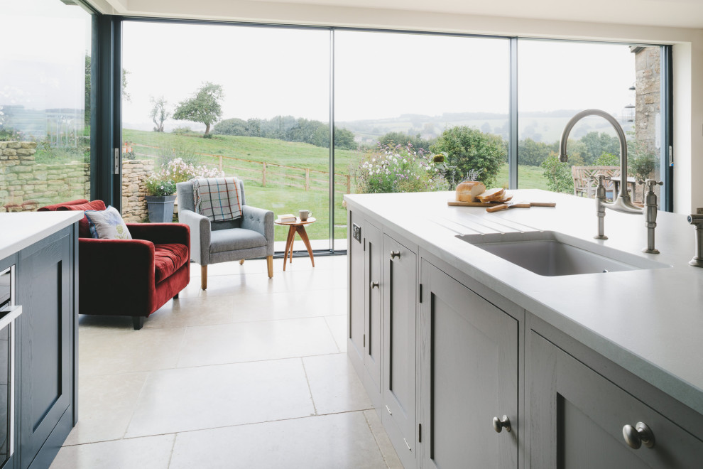 Photo of a large country l-shaped eat-in kitchen in Gloucestershire with a drop-in sink, shaker cabinets, blue cabinets, quartz benchtops, stainless steel appliances, limestone floors, with island and grey benchtop.