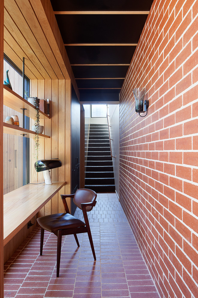 Midcentury home office in Melbourne with red walls, brick floors, a built-in desk and red floor.
