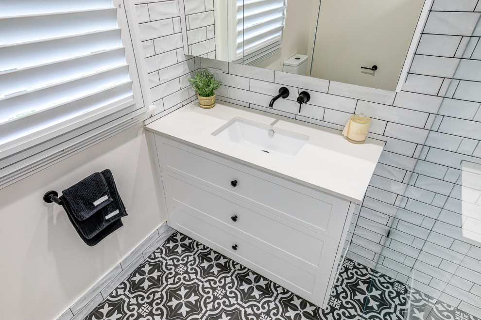 This is an example of a small contemporary bathroom in Brisbane with shaker cabinets, white cabinets, a one-piece toilet, white tile, subway tile, white walls, cement tiles, an undermount sink, engineered quartz benchtops, black floor, a hinged shower door, white benchtops, a niche, a single vanity and a built-in vanity.