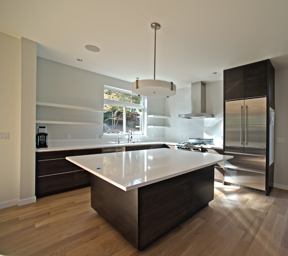 Example of a mid-sized minimalist l-shaped medium tone wood floor open concept kitchen design in Seattle with flat-panel cabinets, black cabinets, quartz countertops, white backsplash, stainless steel appliances and an island