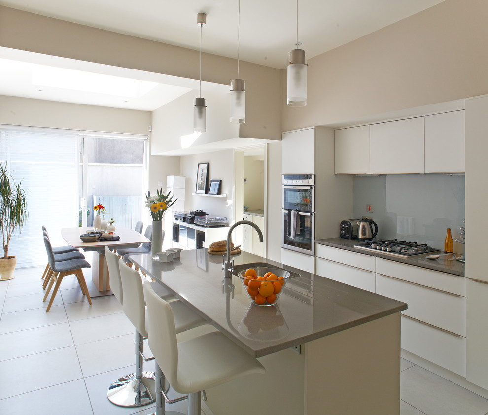Photo of a modern eat-in kitchen in Dublin with an undermount sink, flat-panel cabinets, white cabinets, grey splashback, glass sheet splashback and stainless steel appliances.