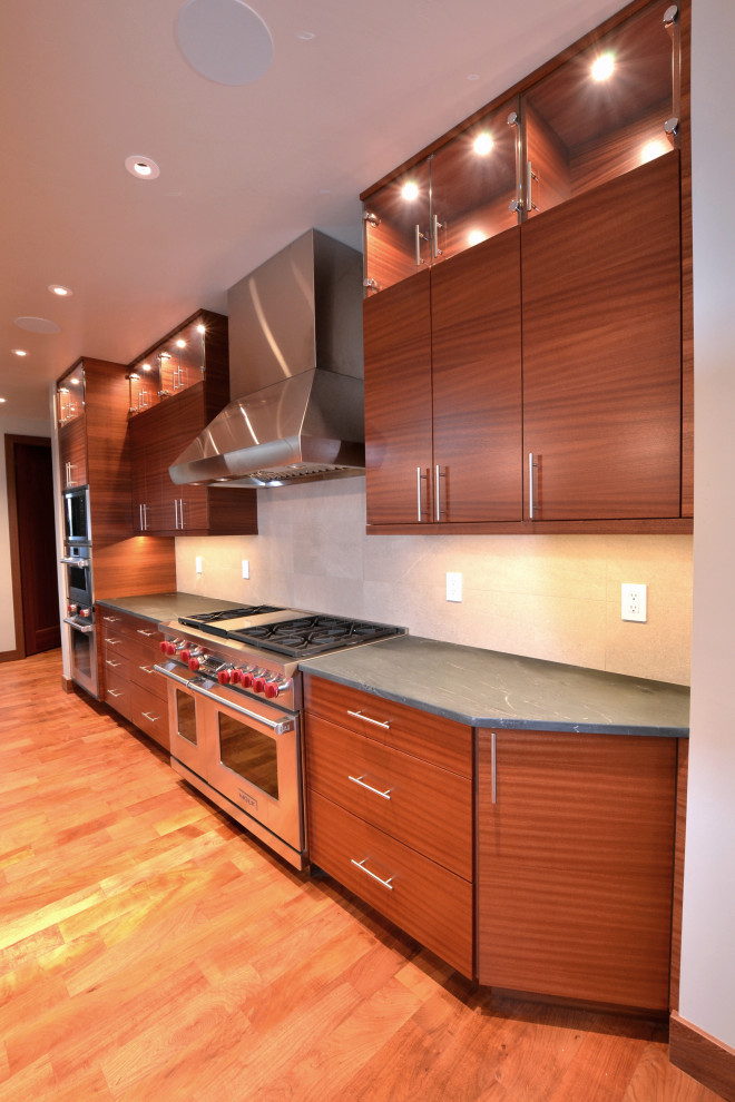 Photo of a large contemporary kitchen in Other with an undermount sink, flat-panel cabinets, red cabinets, soapstone benchtops, beige splashback, stainless steel appliances, medium hardwood floors, with island and grey benchtop.