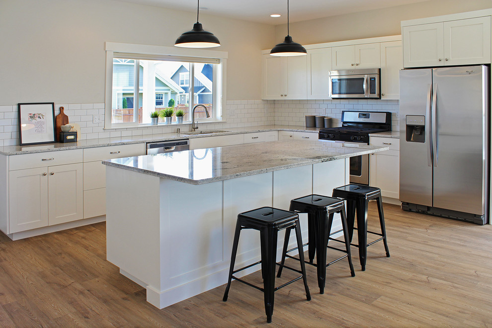 Photo of a large arts and crafts l-shaped open plan kitchen in Seattle with an undermount sink, shaker cabinets, white cabinets, granite benchtops, white splashback, subway tile splashback, stainless steel appliances, vinyl floors and with island.