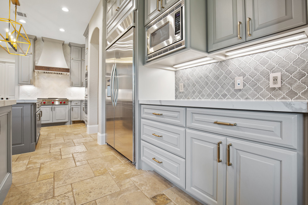Inspiration for a large transitional l-shaped limestone floor and brown floor eat-in kitchen remodel in Houston with a farmhouse sink, beaded inset cabinets, gray cabinets, quartz countertops, gray backsplash, ceramic backsplash, stainless steel appliances, two islands and white countertops