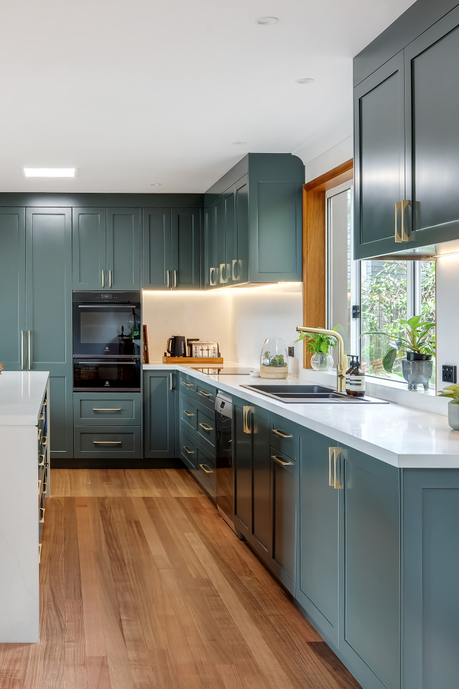 Large transitional l-shaped medium tone wood floor and multicolored floor eat-in kitchen photo in Sydney with a drop-in sink, shaker cabinets, green cabinets, quartz countertops, white backsplash, quartz backsplash, black appliances, an island and white countertops