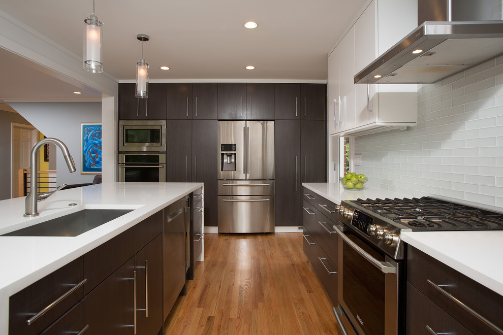 This is an example of a mid-sized contemporary u-shaped open plan kitchen in DC Metro with an undermount sink, flat-panel cabinets, white cabinets, solid surface benchtops, white splashback, subway tile splashback, stainless steel appliances, light hardwood floors and with island.