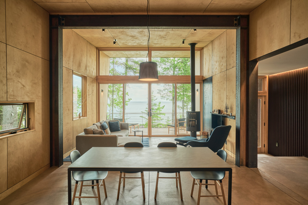 Idee per una sala da pranzo aperta verso il soggiorno stile rurale con pavimento in cemento, stufa a legna, cornice del camino in metallo, soffitto in legno e pareti in legno
