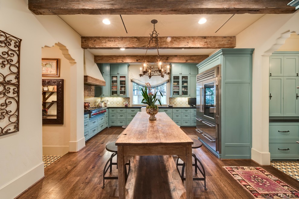 This is an example of a mid-sized mediterranean l-shaped open plan kitchen in Houston with a farmhouse sink, shaker cabinets, blue cabinets, granite benchtops, multi-coloured splashback, cement tile splashback, stainless steel appliances, dark hardwood floors and with island.