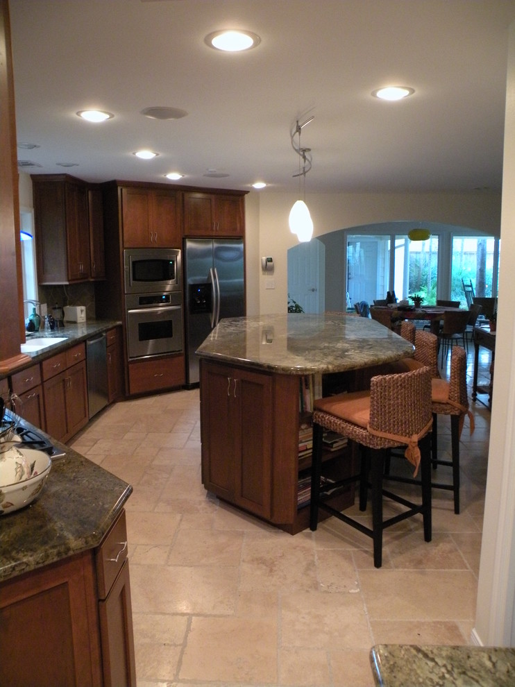 Example of a mid-sized transitional u-shaped limestone floor eat-in kitchen design in Houston with an undermount sink, shaker cabinets, medium tone wood cabinets, granite countertops, beige backsplash, ceramic backsplash, stainless steel appliances and an island